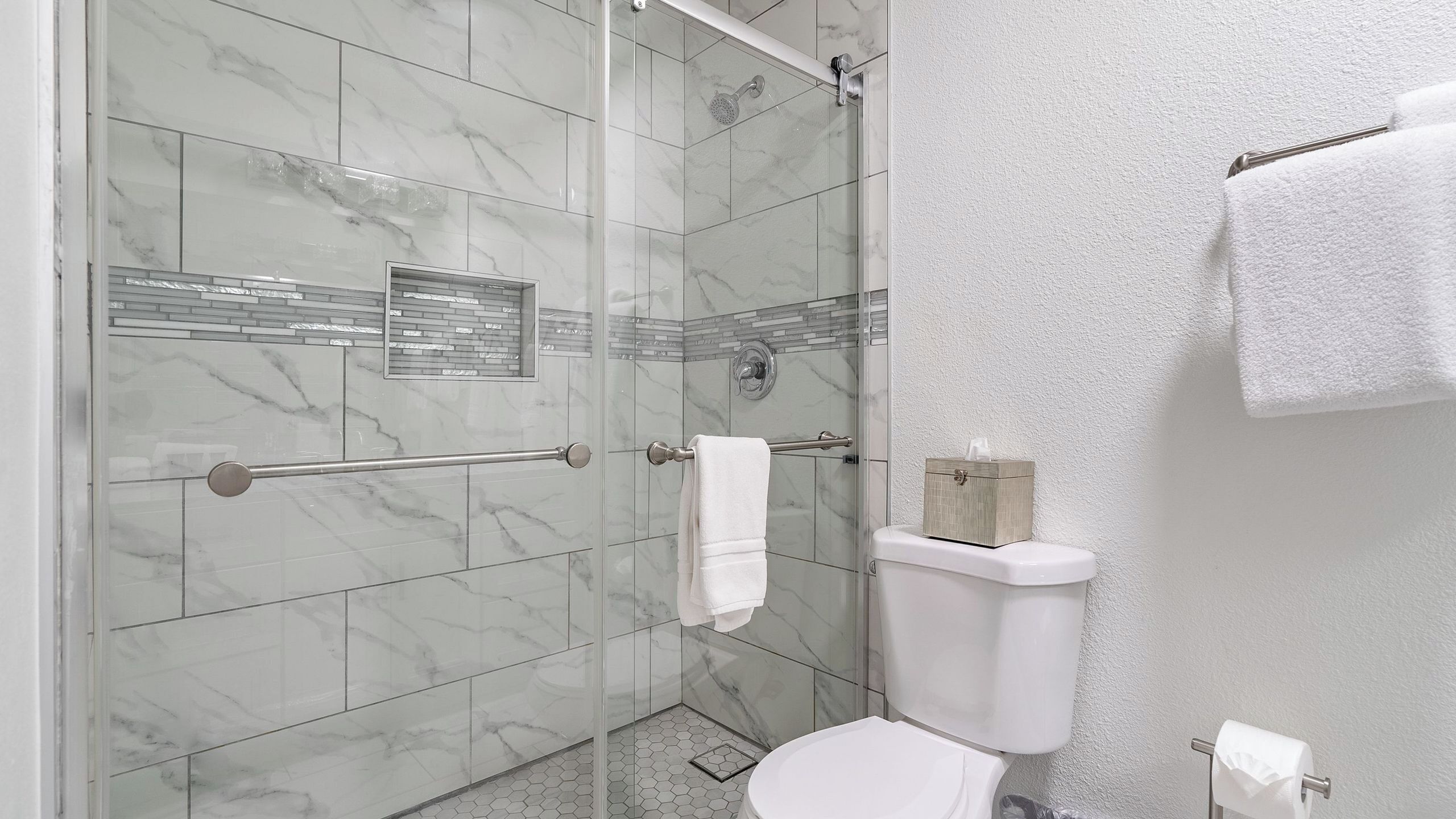 Een badkamer met een douchecabine van glas, een toilet en een handdoekhouder.