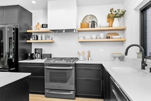 A modern kitchen with black cabinetry, a stainless steel refrigerator, a built-in oven, and a black faucet. - Fern + Cedar Cabin | hot tub | fireplace | firepit (Deming)