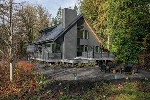 A modern house with a sloped roof, large windows, and a deck with outdoor seating. - Modern Architect's Cabin w/ Hot Tub, Sleeps 12 (Deming)