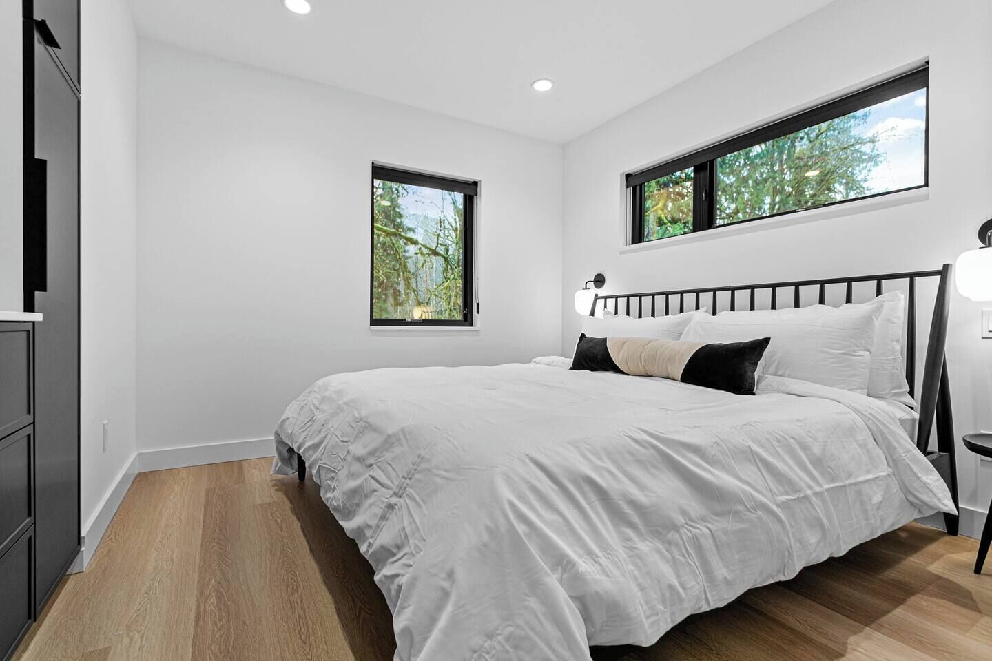 Une chambre à coucher avec un lit, deux fenêtres, une table de chevet et une commode.