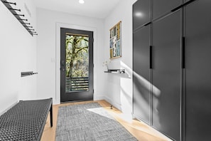 A modern interior with a dark door, a bench, a rug, and a large wardrobe. - Fern + Cedar Cabin | hot tub | fireplace | firepit (Deming)