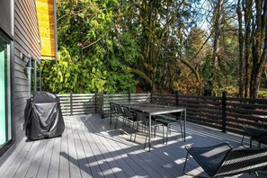 Una terraza con mesa y sillas, rodeada por una valla de madera y abundante follaje.