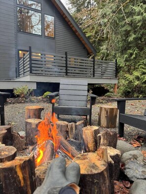 A fire pit with logs in front of a modern house with a deck. - Modern Architect's Cabin w/ Hot Tub, Sleeps 12 (Deming)