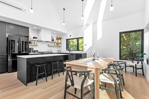 A modern kitchen with a central island, black bar stools, and a dining area with a wooden table and chairs. - Fern + Cedar Cabin | hot tub | fireplace | firepit (Deming)