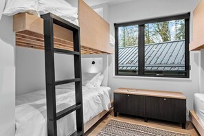 A bunk bed with a wooden ladder and a desk with a book, a window with a view of the roof, and a patterned rug on the floor. - Fern + Cedar Cabin | hot tub | fireplace | firepit (Deming)