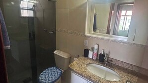 Ein Badezimmer mit einer Duschkabine, einer Toilette, einem Waschbecken mit Spiegel darüber und einem Teppich mit Muster.