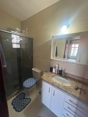 Ein Badezimmer mit einer Duschkabine, einer Toilette, einem Waschbecken mit Spiegel darüber und einem Teppich mit Muster.