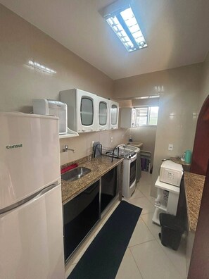 A compact kitchen with a refrigerator, a microwave, a gas stove, and a sink. - Apartment for rent in Cabo Frio (Cabo Frio)