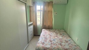 Ein kleines Schlafzimmer mit einem Bett, einem Fenster mit Vorhängen, einem Deckenventilator und einer Klimaanlage.