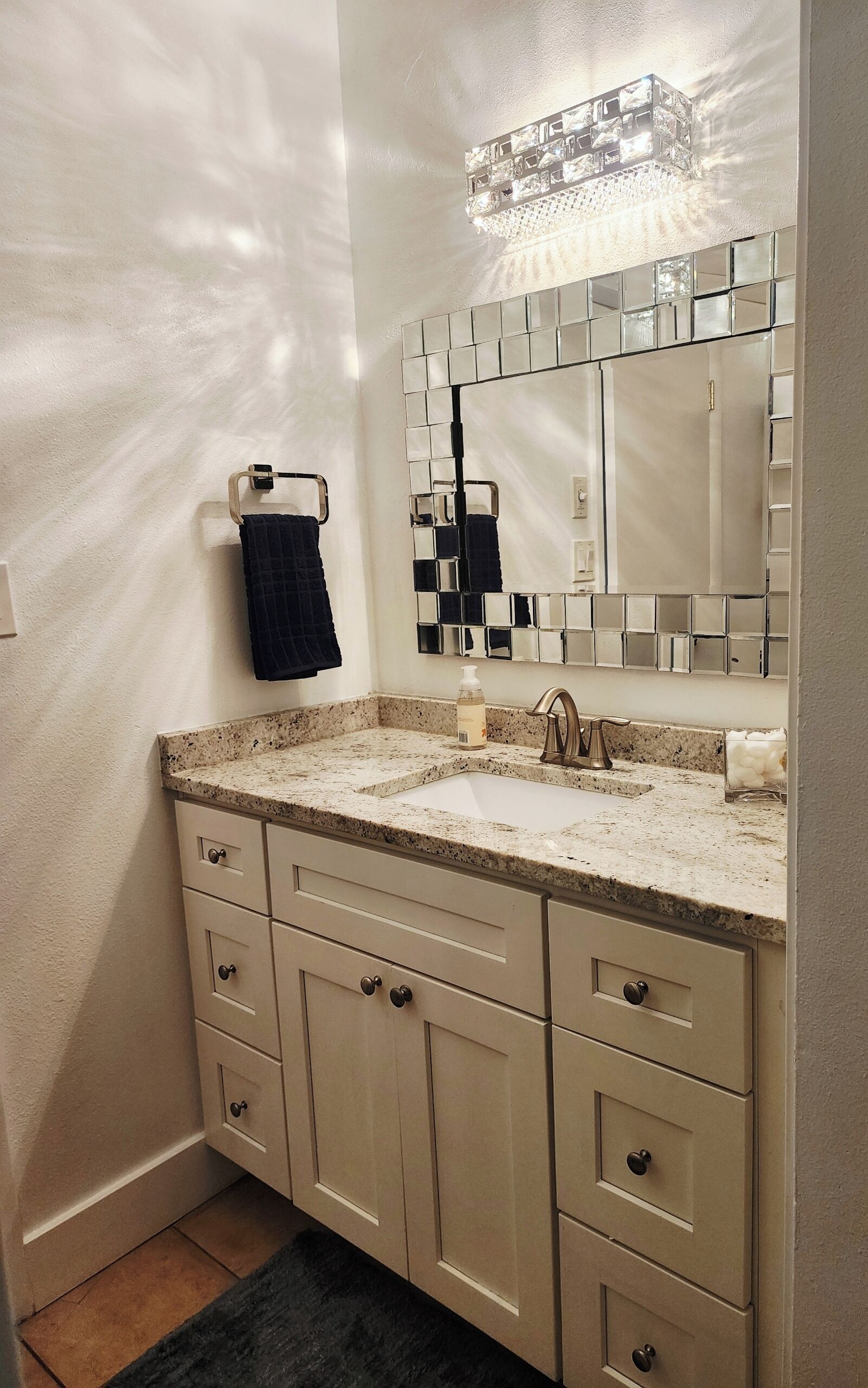 Une salle de bain avec un comptoir en granit, un lavabo, un miroir et un porte-serviettes.