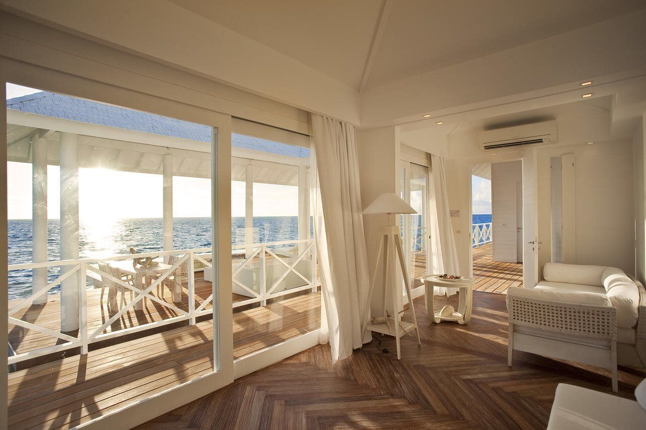 Amplia habitación con una gran ventana con vistas al mar, un sofá blanco, una mesita y una lámpara.