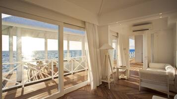Amplia habitación con una gran ventana con vistas al mar, un sofá blanco, una mesita y una lámpara.