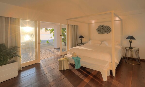 Un dormitorio con cama con dosel, vista al mar por la puerta y una mesita de noche con lámpara.
