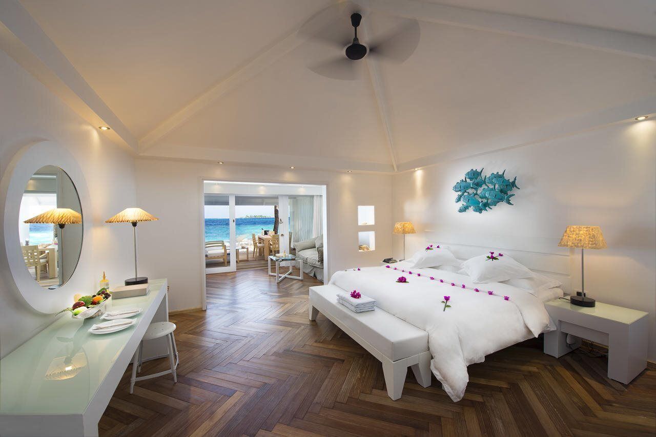 Habitación de hotel con cama, mesitas de noche, un escritorio, un espejo y vista al mar.