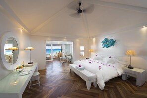 Habitación de hotel con cama, mesitas de noche, un escritorio, un espejo y vista al mar.