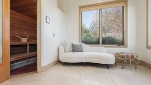 A room with a white sofa, a wooden bench, a window with a view of trees, and a tiled floor. - The Estate Villa at Dresser Winery by Avantstay Pool + Sauna Paso Robles (Paso Robles)