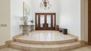 A spacious foyer with a marble staircase, a chandelier, a wooden door with glass panels, and a framed artwork on the wall. - The Estate Villa at Dresser Winery by Avantstay Pool + Sauna Paso Robles (Paso Robles)
