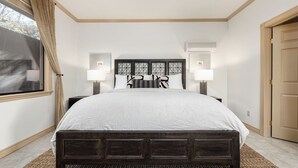 A bedroom with a large bed, two bedside lamps, a window with curtains, and an air conditioning unit. - The Estate Villa at Dresser Winery by Avantstay Pool + Sauna Paso Robles (Paso Robles)