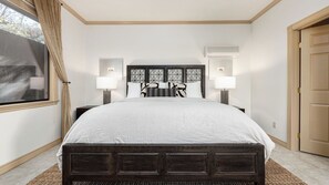 Ein Schlafzimmer mit einem großen Bett, zwei Nachttischlampen, einem Fenster mit Vorhängen und einer Klimaanlage.
