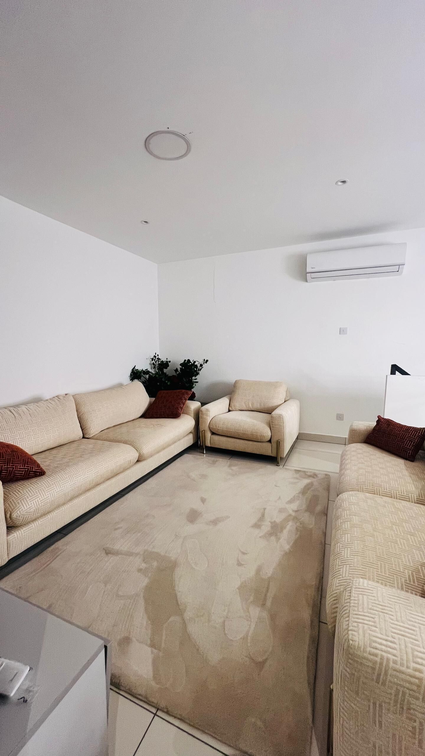 A living room with a beige sectional sofa, a small table, and a potted plant.