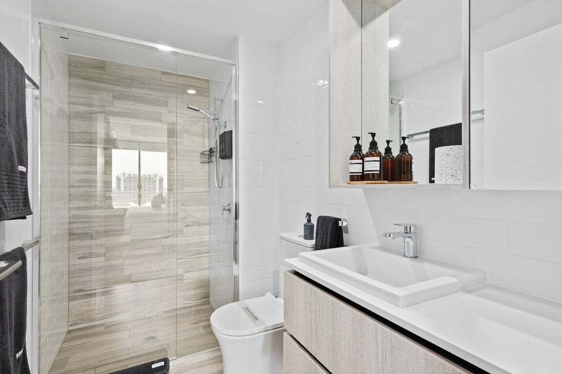 A modern bathroom with a glass-enclosed shower, a white sink, and a large mirror.