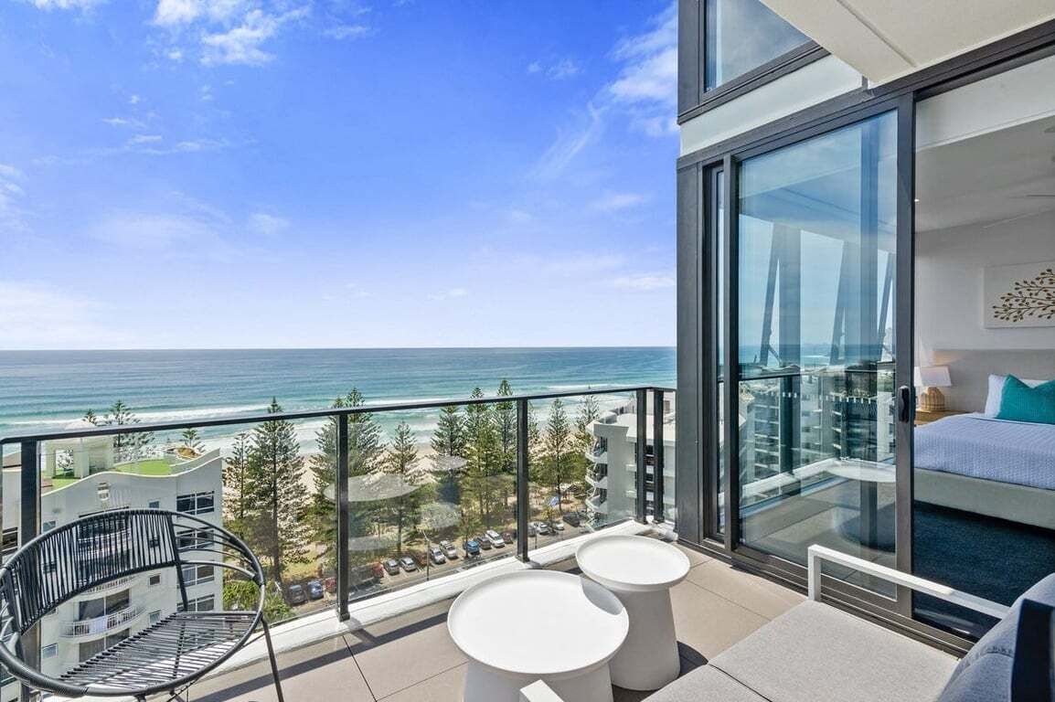 A balcony with a view of the ocean, a bed, and a chair.