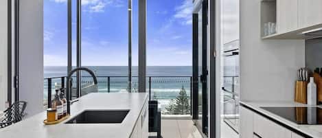 Una cocina moderna con un amplio ventanal con vista al mar, horno empotrado y pileta.