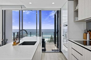 A modern kitchen with a large window overlooking the sea, a built-in oven, and a sink. - Sandbar Burleigh - Ocean Delight (Gold Coast)