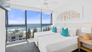 A bedroom with two beds, a ceiling fan, a large window with a view of the ocean, and a wall-mounted artwork. - Sandbar Burleigh - Ocean Delight (Gold Coast)
