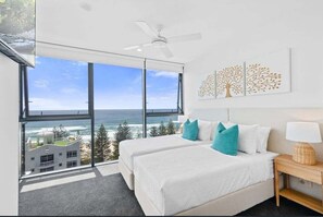 Ein Schlafzimmer mit zwei Betten, einem Deckenventilator, einem großen Fenster mit Meerblick und einem Wandbild.
