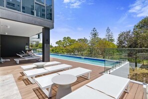 Un área de piscina moderna al aire libre con sillones de descanso y barandilla de vidrio.