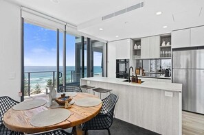 Eine moderne Küche mit Meerblick, ein Essbereich mit rundem Tisch und Stühlen sowie ein Balkon ebenfalls mit Meerblick.
