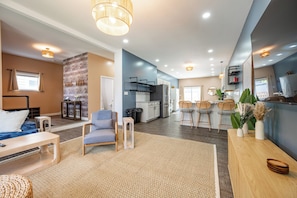 A modern living room with a sofa, a coffee table, and a dining area with chairs. - Indy Grand House - 6BR - Hot Tub - Game Room (Indianapolis)