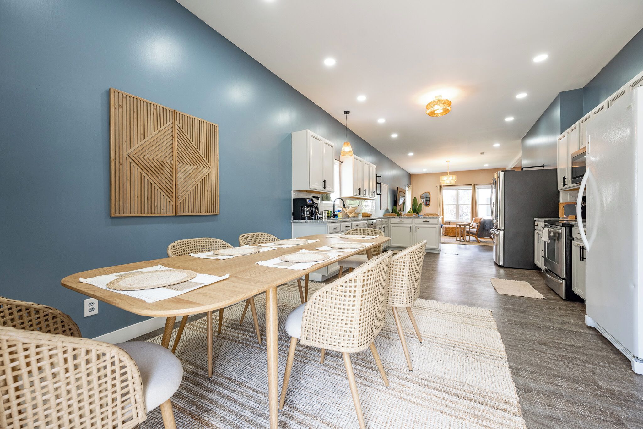 A modern kitchen with white cabinets, a stainless steel refrigerator, and a dining area with a wooden table and wicker chairs.