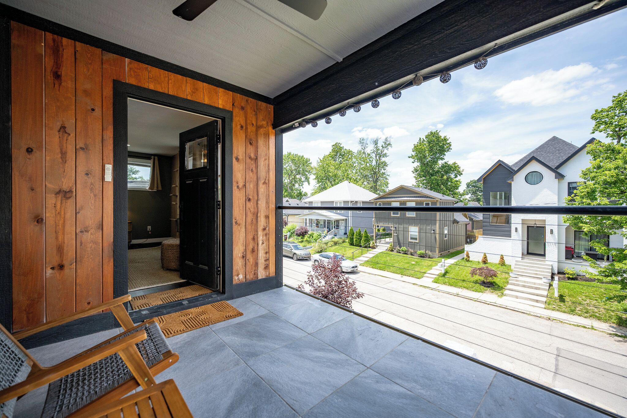 A modern home interior with a balcony, wooden walls, and a view of neighboring houses.
