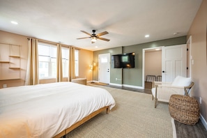 A bedroom with a large bed, a ceiling fan, a TV, and a door leading to another room. - Indy Grand House - 6BR - Hot Tub - Game Room (Indianapolis)