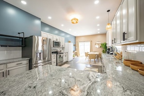 A modern kitchen with granite countertops, stainless steel appliances, and a dining area with wicker furniture. - Indy Grand House - 6BR - Hot Tub - Game Room (Indianapolis)