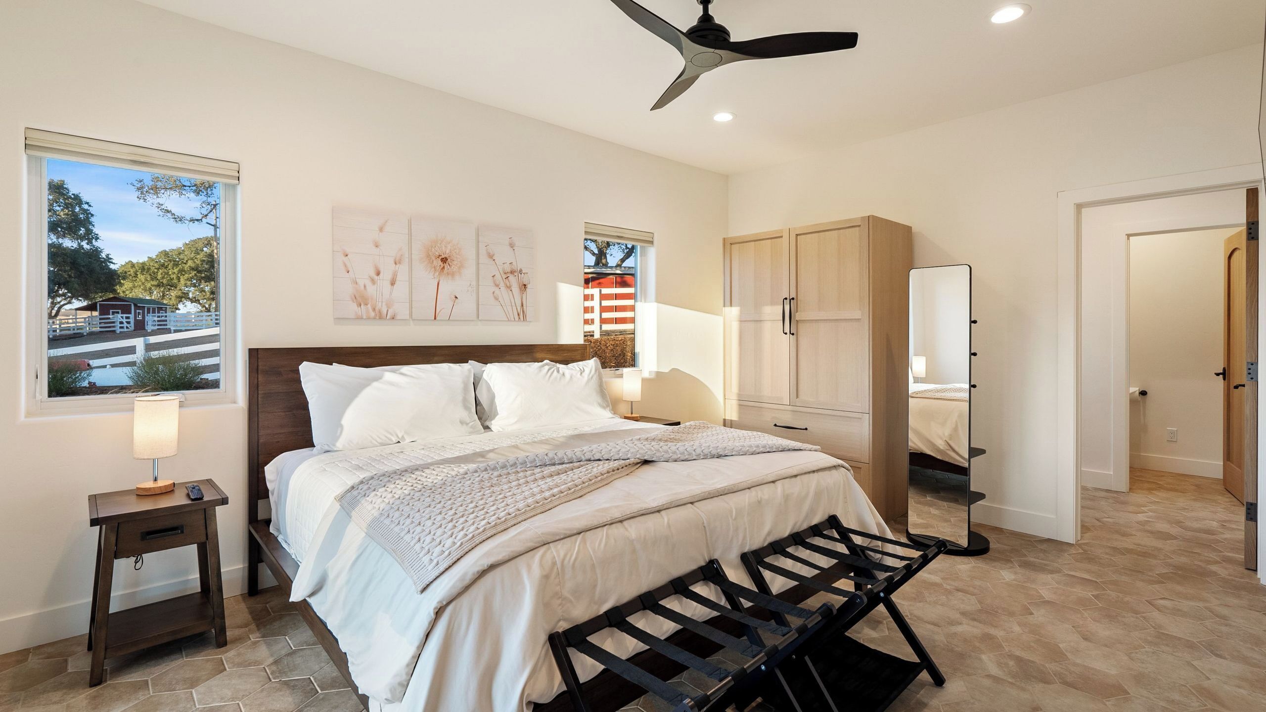 A bedroom with a bed, bedside table, lamp, and a view of a barn through a window.