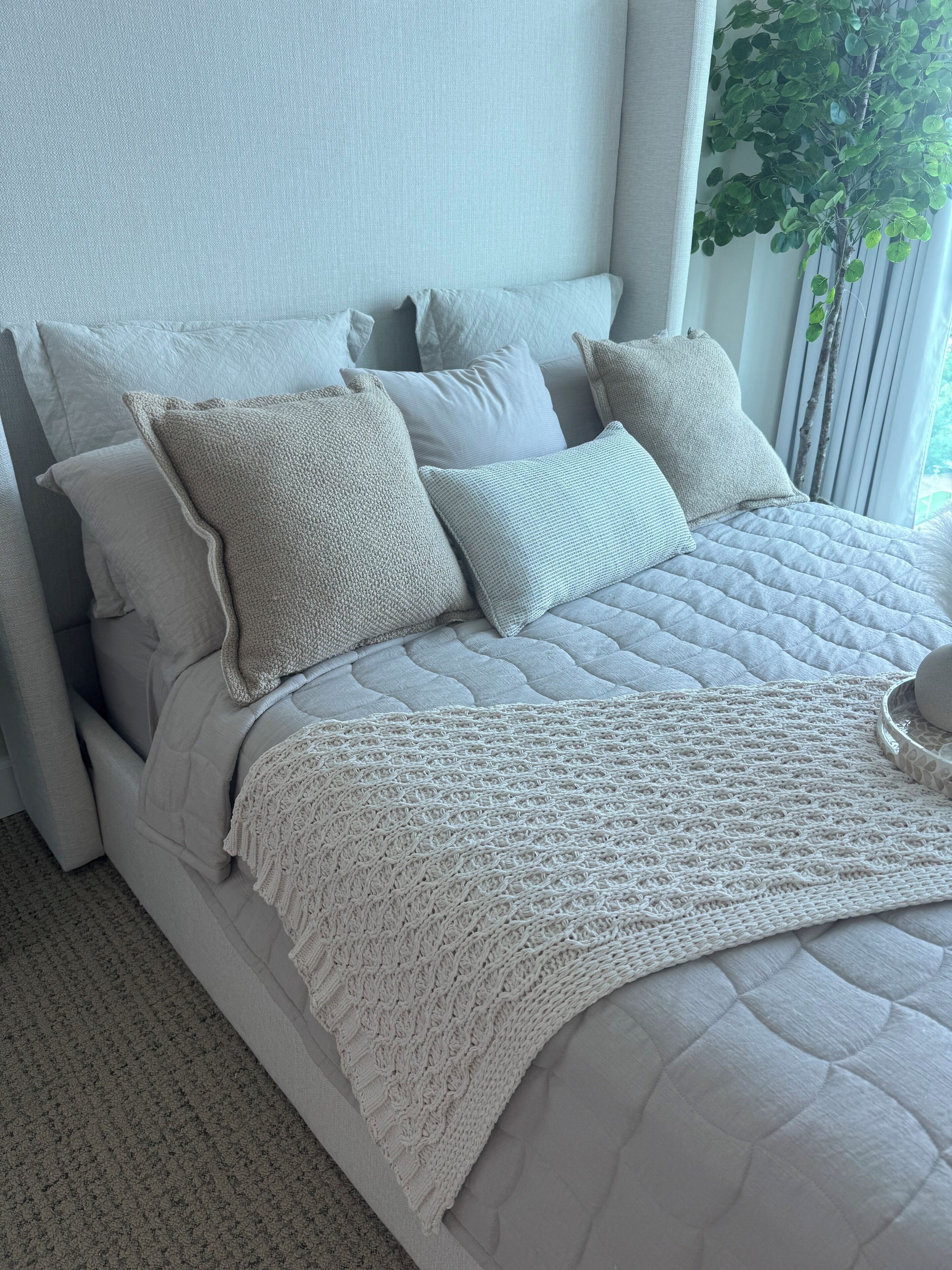 A bed with a quilted headboard, multiple pillows, and a knitted throw.