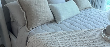 A bed with a quilted headboard, multiple pillows, and a knitted throw.