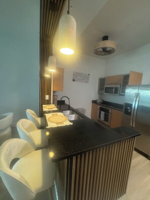 A modern kitchen with a central island, stainless steel appliances, and a dining area with white chairs. -  Pier-fect Day 2 bedroom condo in Ft Myers (Fort Myers)