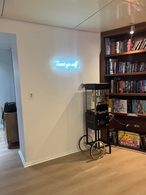 Une pièce avec un panneau néon sur lequel on peut lire « Faites-vous plaisir », une bibliothèque remplie de livres et un chariot à bicyclette d’époque.