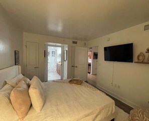 Quarto com cama, televisão fixada na parede e porta para outro cômodo.