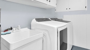 Une buanderie équipée de deux machines à laver à chargement frontal, d’un évier et de placards.