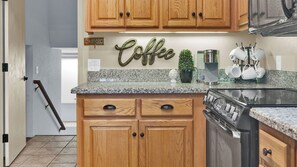 A kitchen with wooden cabinets, a granite countertop, a coffee sign, a coffee maker, and a stove. - Naci Lakeview Retreat by Avantstay Game Room + Bar + Lake Views Gated Marina, Ramps + Pool (Bradley)