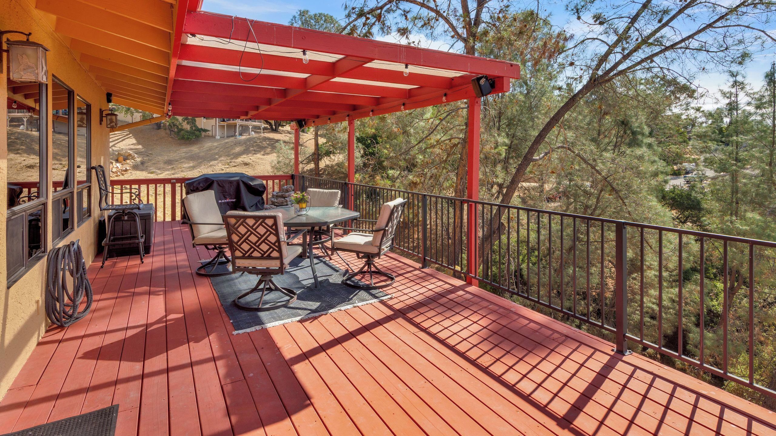 A covered outdoor patio with a table and chairs, a grill, and a view of the surrounding trees.