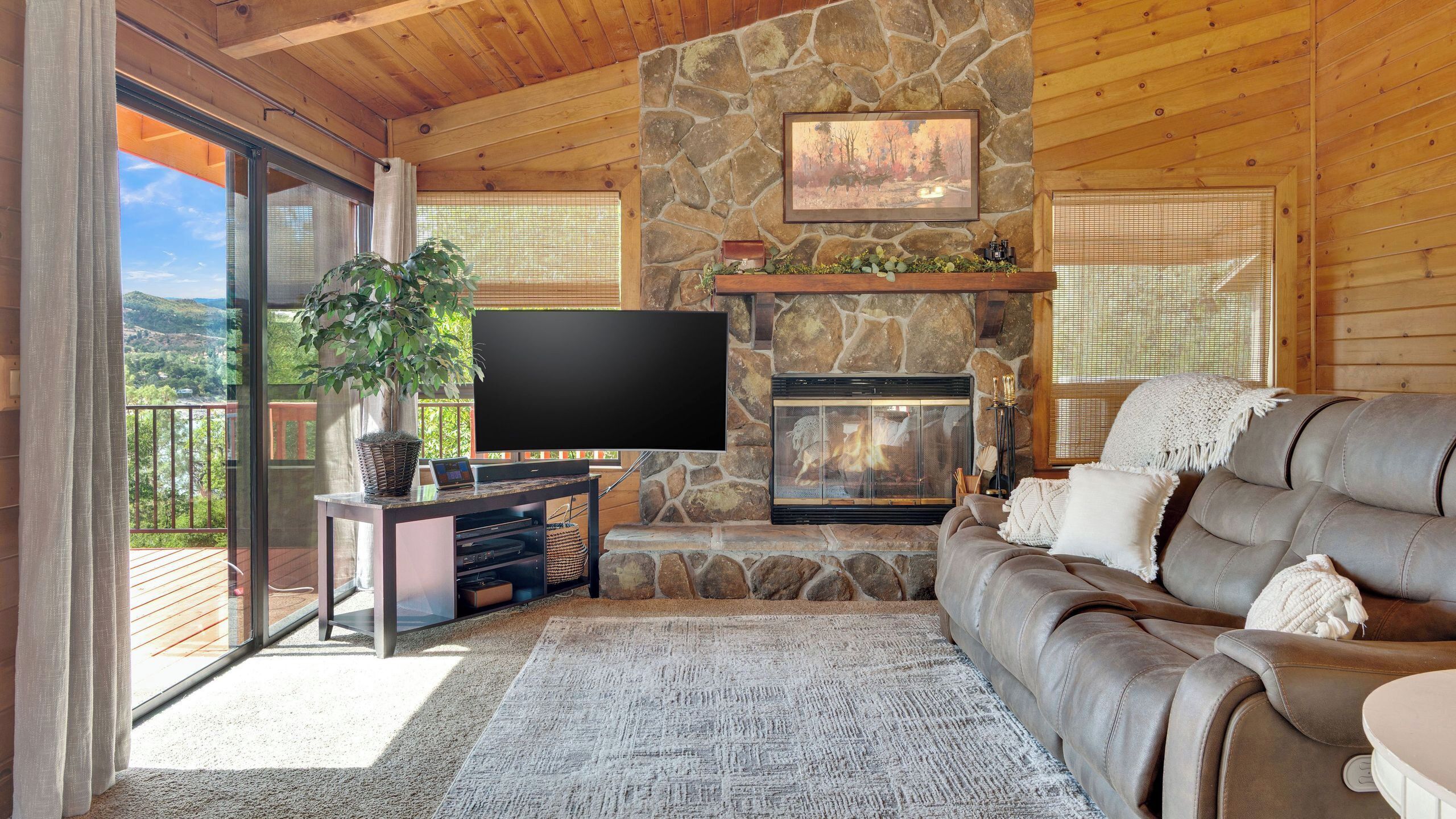 A cozy living room with a stone fireplace, a flat-screen TV, and a leather sofa.