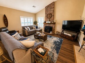 Un salon comprenant un canapé, une table basse, une cheminée, un téléviseur et une grande fenêtre.