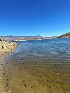 A clear lake with a rocky shoreline and distant mountains under a blue sky.
