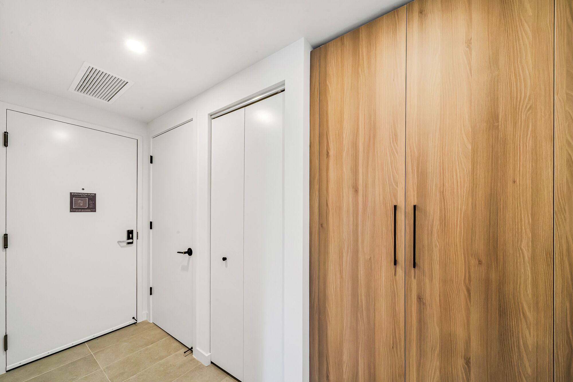 A hallway with white doors, a wooden wardrobe, and a ceiling vent.